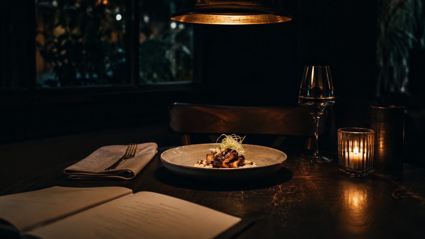 Candle-lit Berlin restaurant table at night, plated dish under brass cutlery and a single tungsten pendant